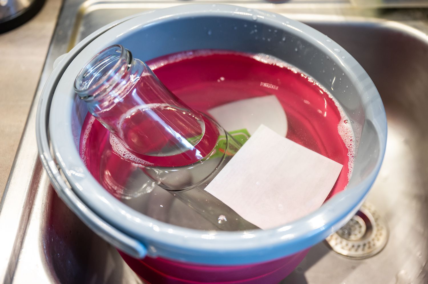 submerging glass with a label into a bucket of warm sudsy water