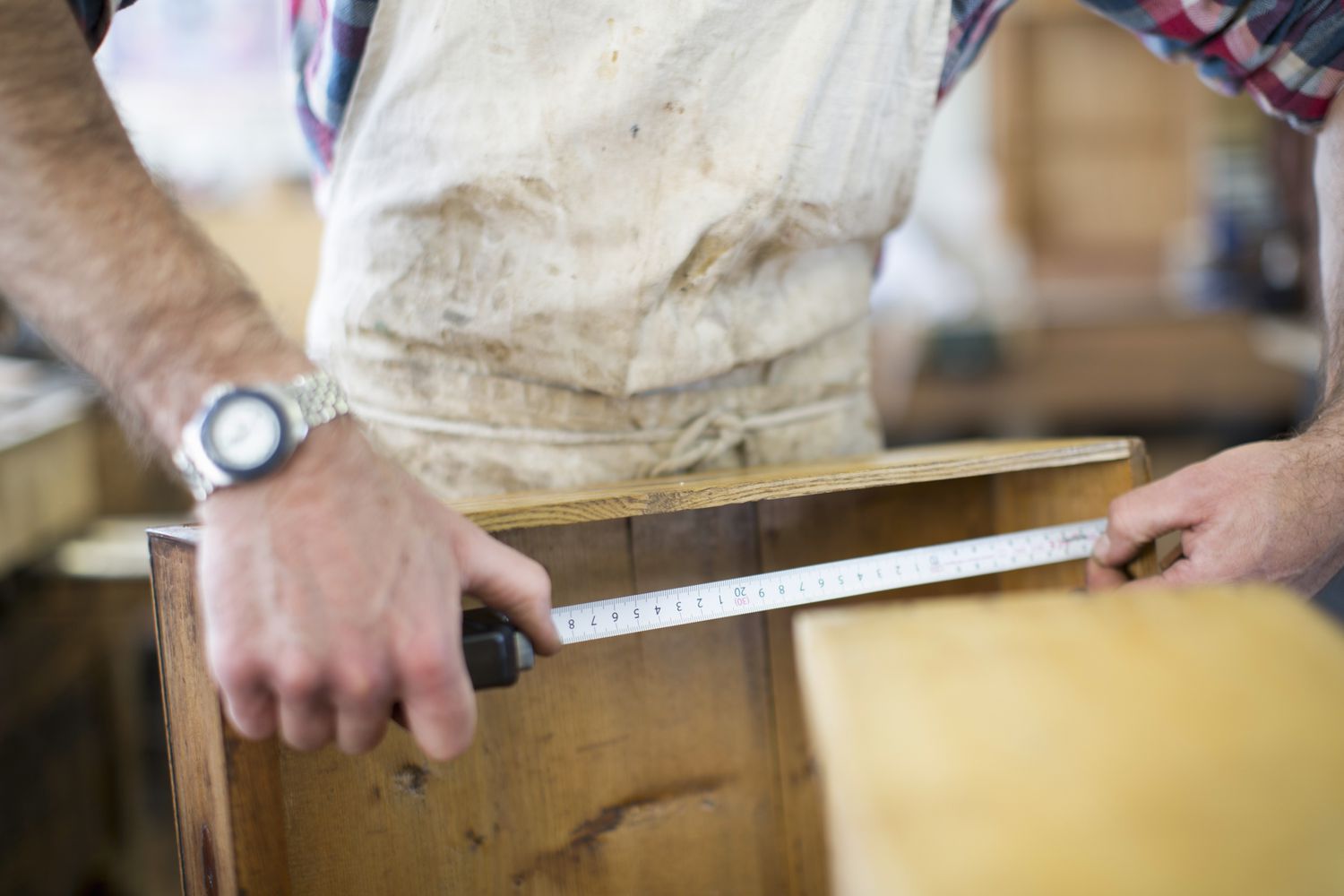 Ein Restaurator für antike Möbel misst ein Stück Holz aus.