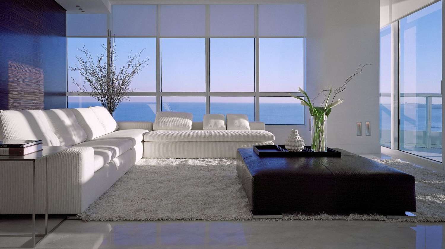 Streiflichter werfen Licht in ein Wohnzimmer mit bodentiefen Fenstern, weißen Sofas und braunem Hocker.