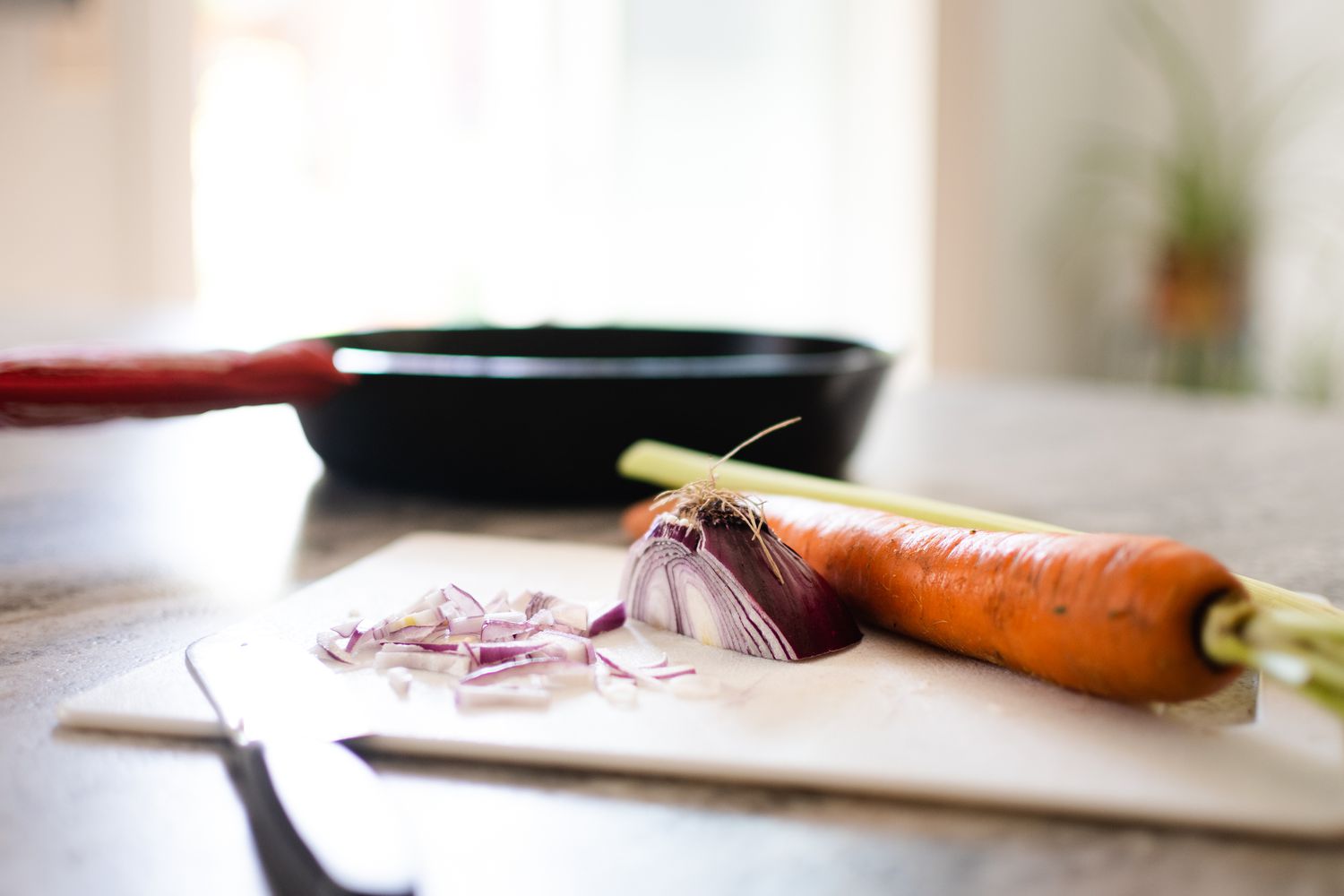 Bratpfanne hinter einem Schneidebrett mit geschnittener Karotte und Zwiebel neben dem Messer