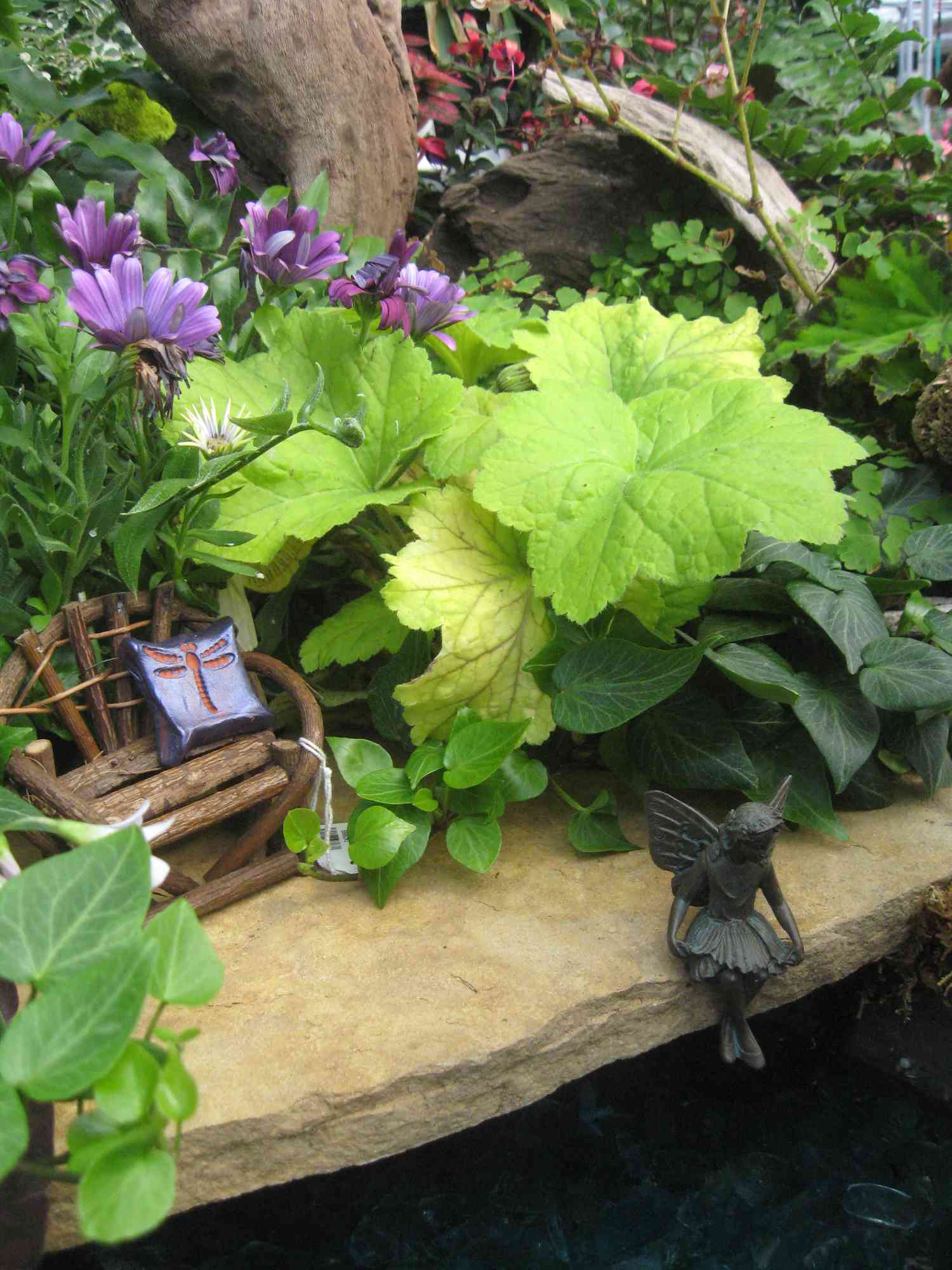 Banco em miniatura e estátua de fada entre plantas.