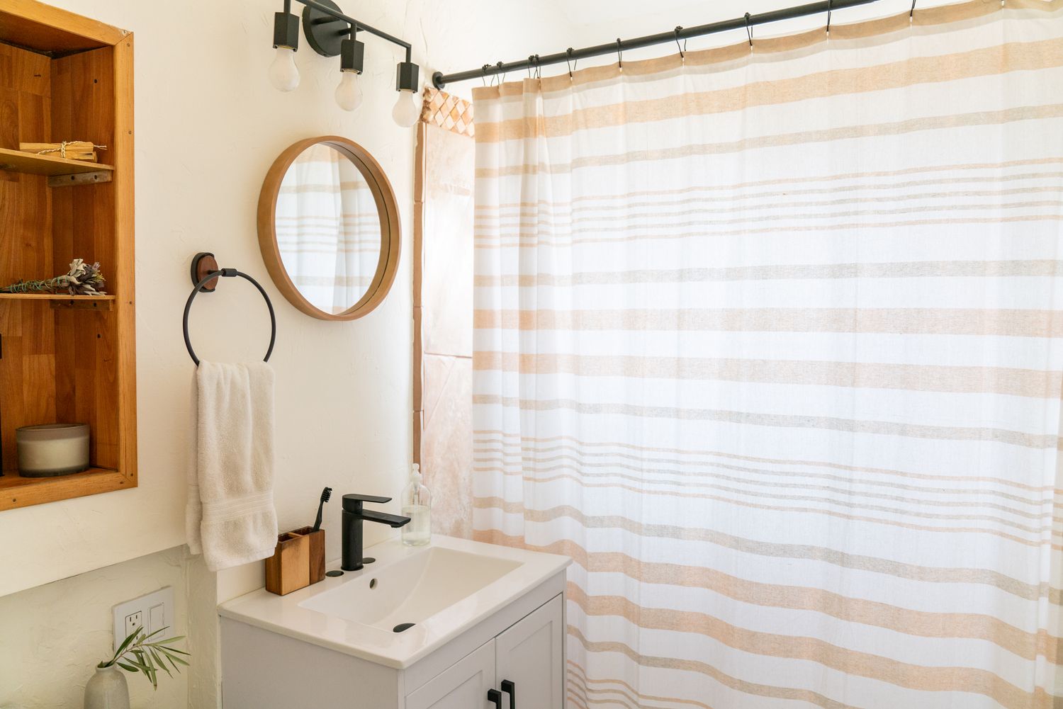 Petite salle de bain avec petit miroir rond à côté d'un rideau de douche blanc et tan
