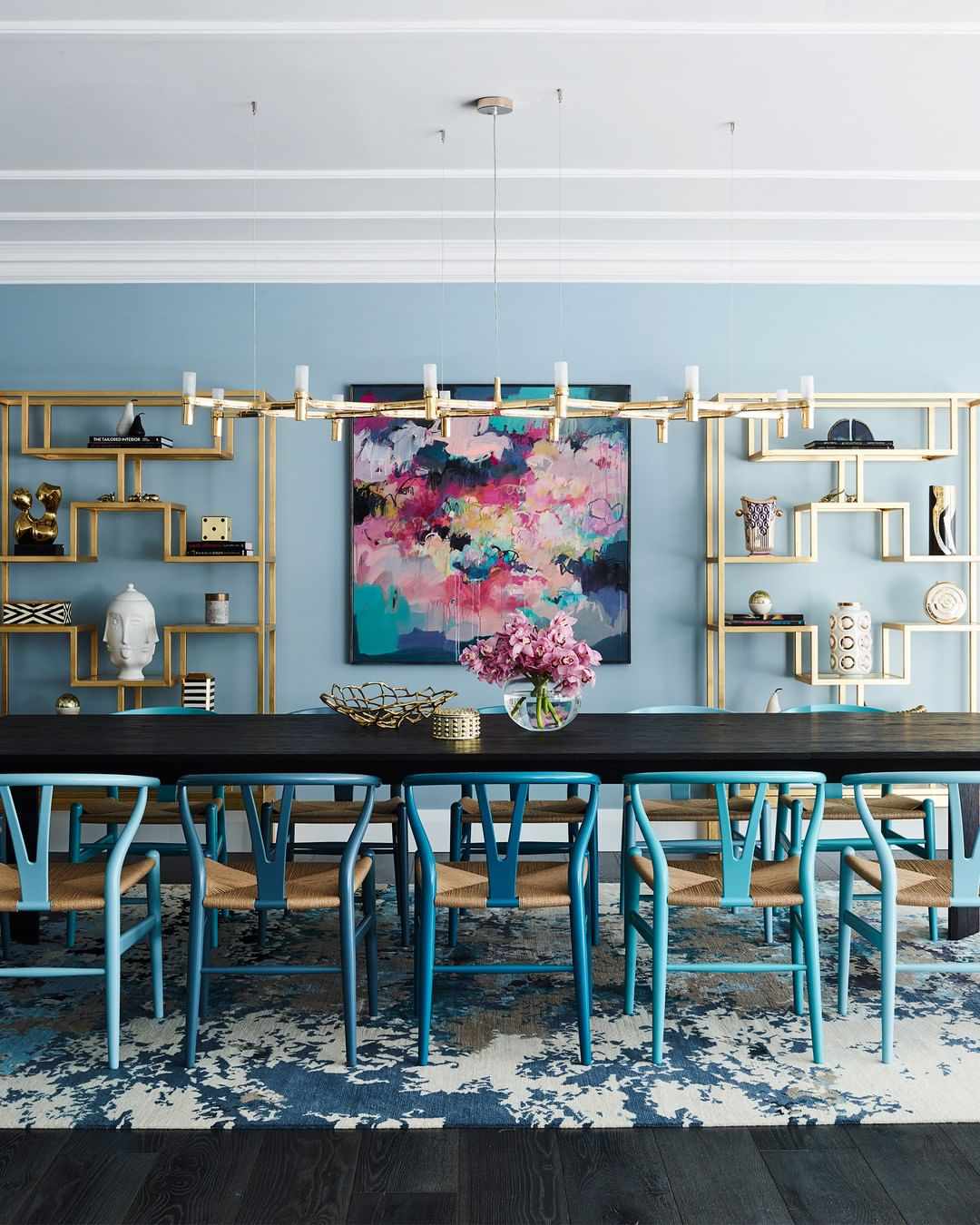 Table à manger avec des chaises bleues et une bibliothèque dorée