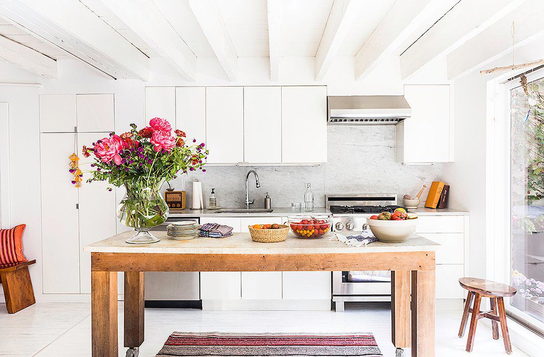 cozinha branca com detalhes em madeira e um grande buquê sobre a mesa 