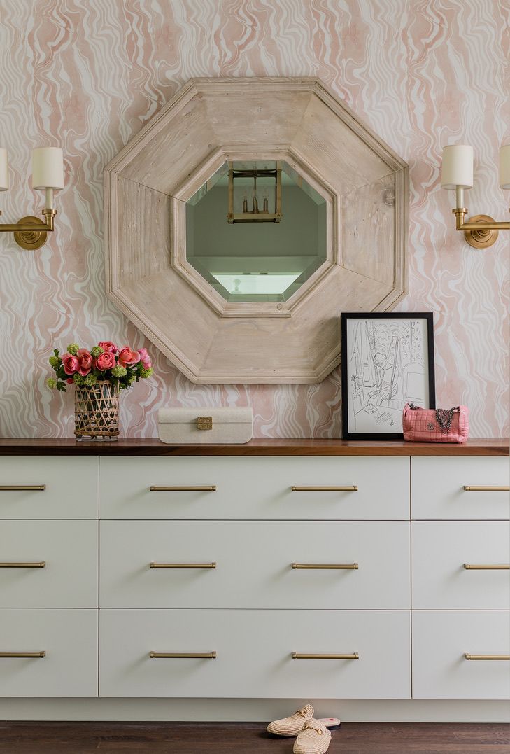 Rosa Wirbel-Tapete gibt in diesem Schlafzimmer mit weißer Kommode, Wandleuchtern und frischen Blumen den Ton an