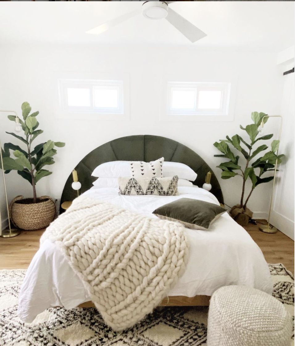 Neutrales Schlafzimmer mit Pflanzen, klobiger gewebter Decke, halbkreisförmigem Kopfteil