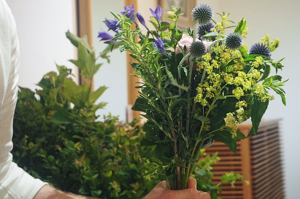 Person mit selbstgebundenem Blumenstrauß aus Grünzeug