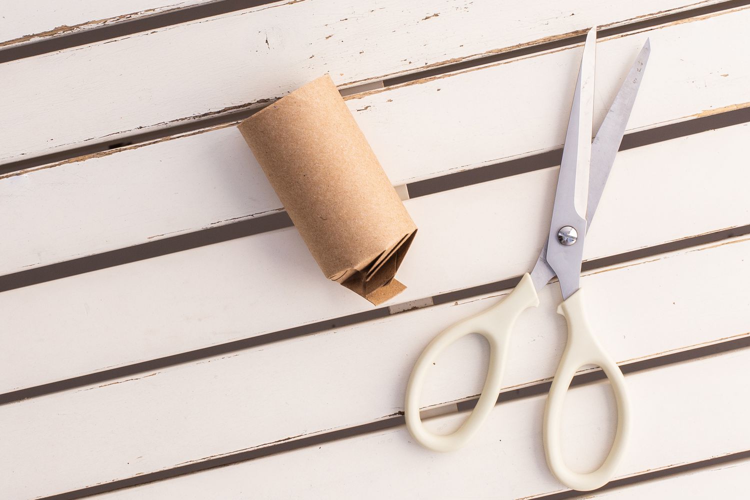 Toilettenpapierrolle über das Ende gefaltet neben einer Schere auf einer weißen Holzfläche