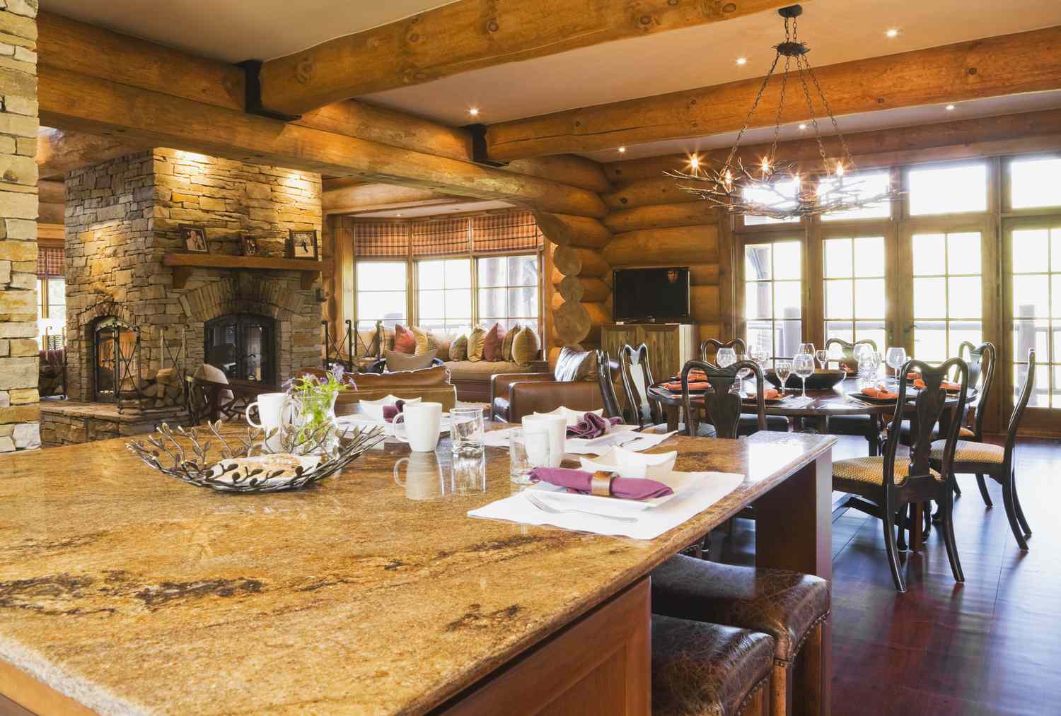 Isla con encimera de granito en la cocina y mesa de comedor redonda de madera con 8 sillas en el interior de una lujosa casa de troncos estilo cottage, Quebec, Canadá.