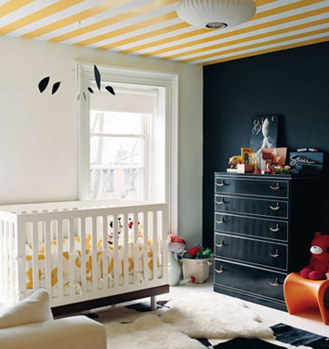 Quarto de bebê com parede de destaque azul-marinho e teto listrado de amarelo