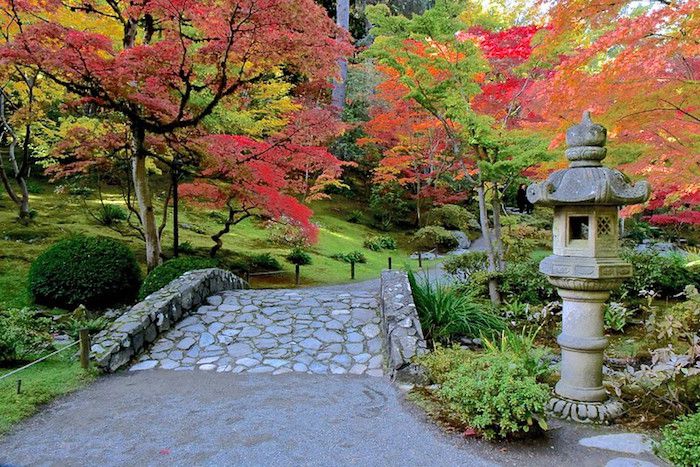 Steinweg und steinerne Tempelskulptur im Garten mit roten japanischen Ahornbäumen.