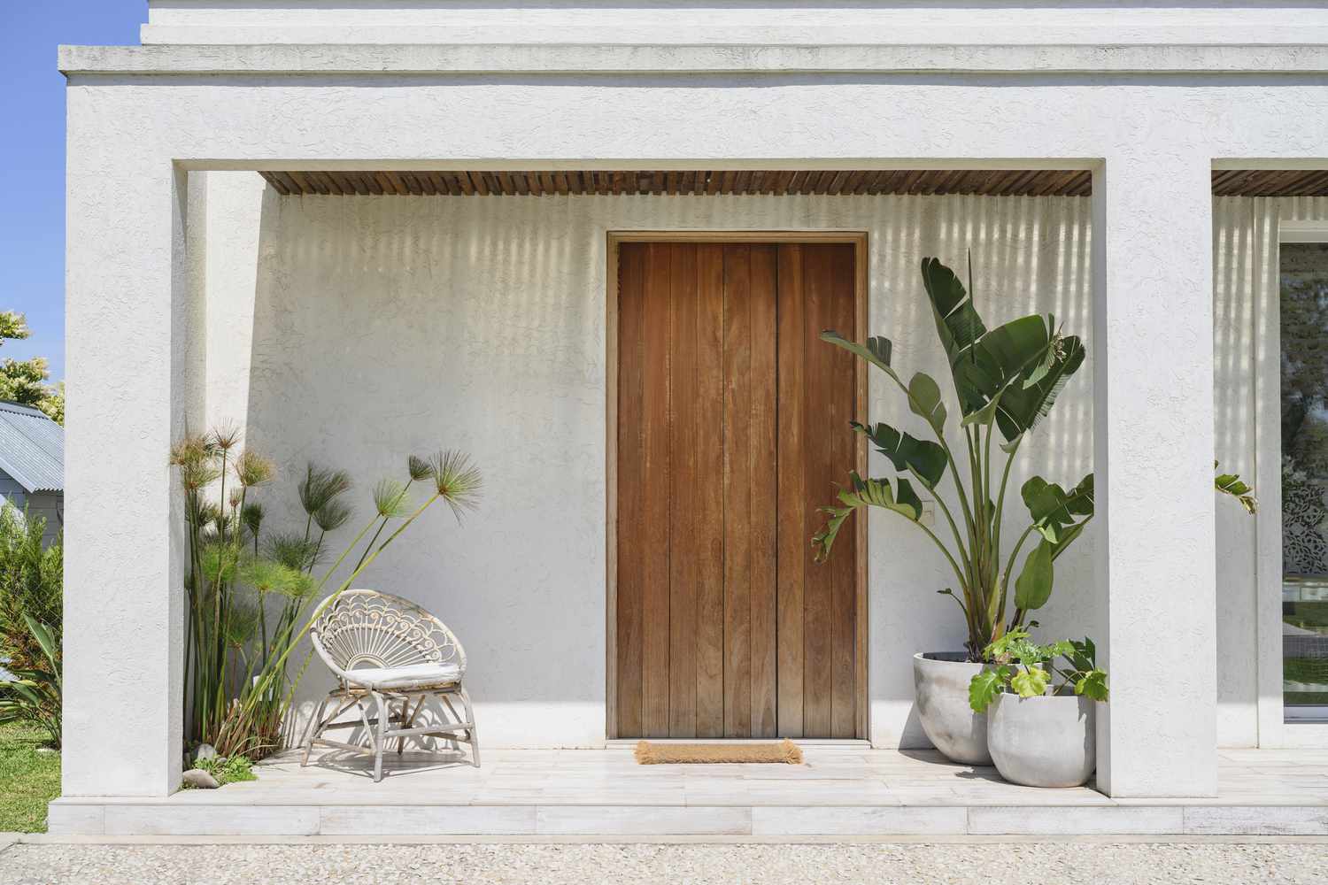Primer plano de la entrada de una casa moderna de Buenos Aires con una silla y plantas en macetas en el porche a ambos lados de la puerta principal.