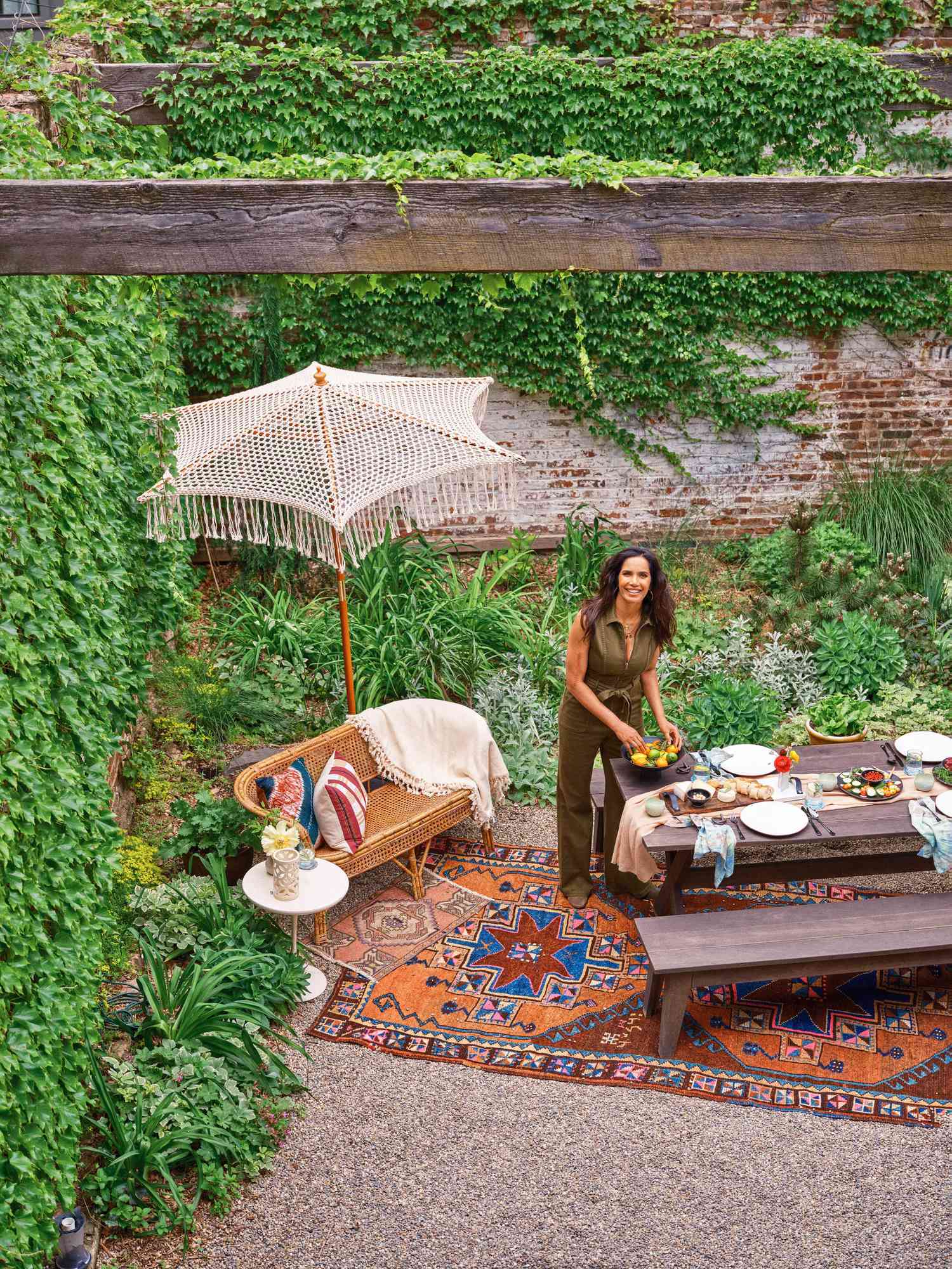 Padma pose à l'extérieur avec une table à manger, un canapé et de beaux accessoires, y compris des tapis, un parapluie, et des coussins jetables