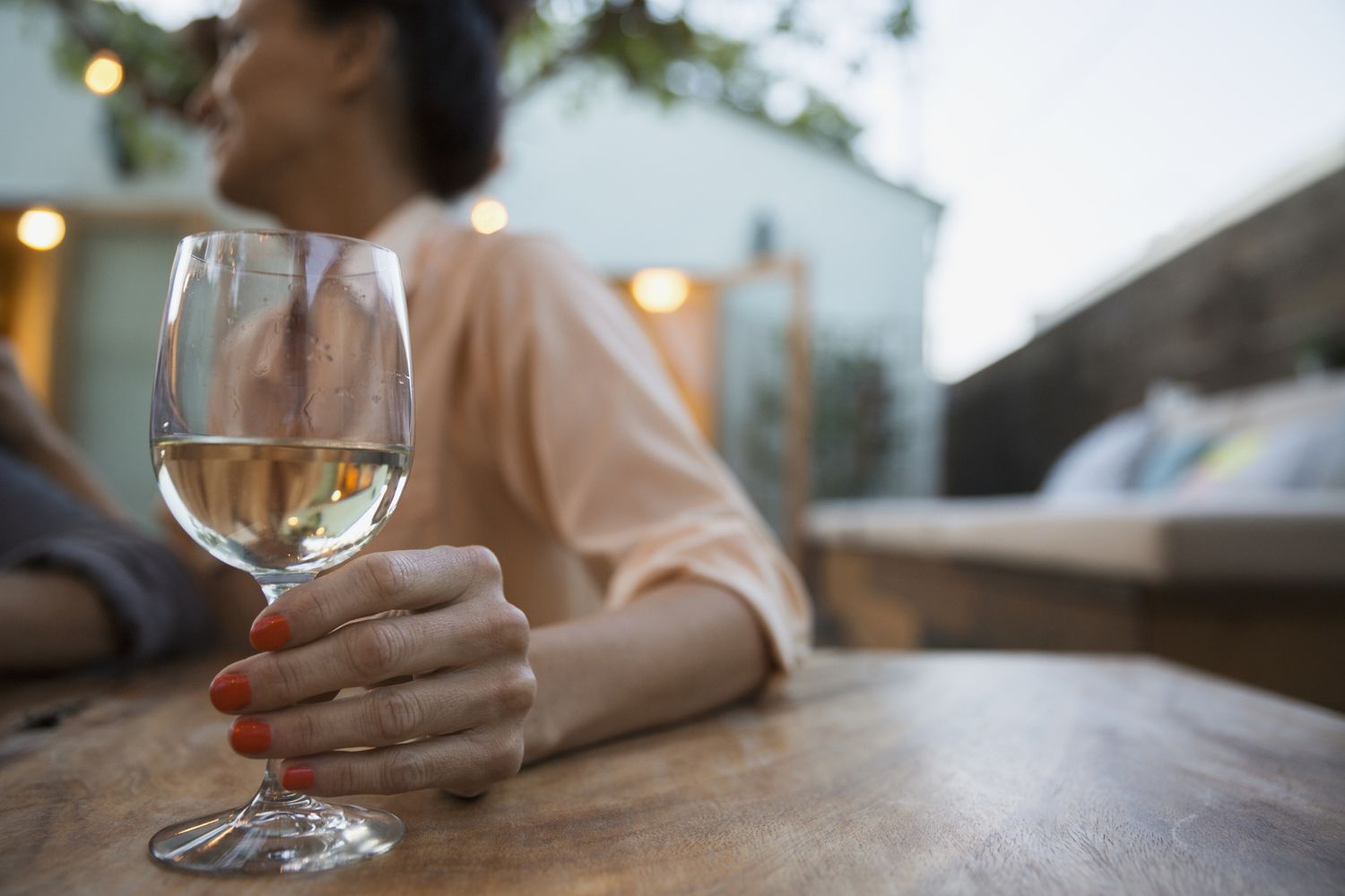 Une personne tenant un verre de vin blanc assise à une table extérieure