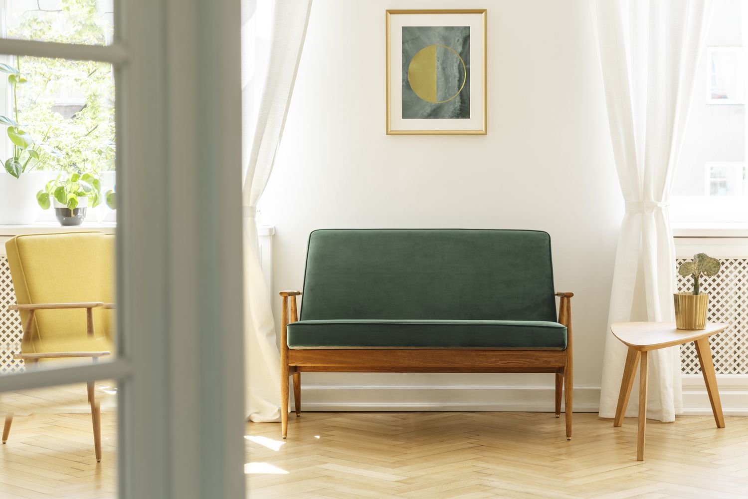 Pôster acima do sofá de madeira verde no interior de uma sala de estar vintage com mesa branca