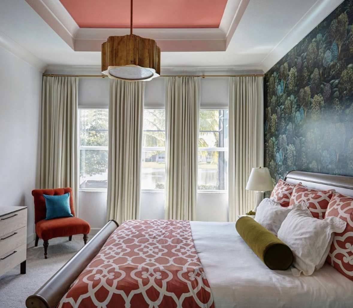 dormitorio con papel pintado en azul y verde, colcha y almohadas en rojo patten, silla roja con almohada azul sólido en la esquina