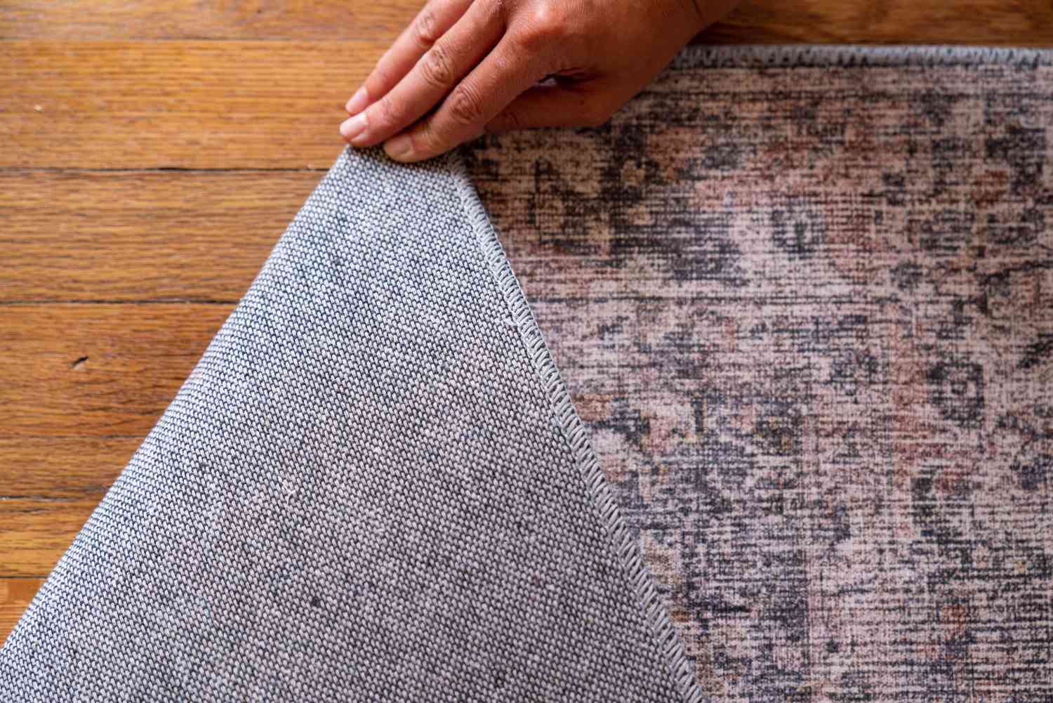 Hellrosa, hellbrauner und grauer handgetufteter Teppich, der umgedreht wird, um das maschinelle und handgefertigte Muster zu zeigen