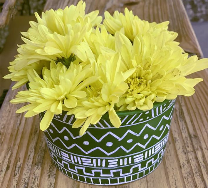 Una maceta pintada de verde con flores amarillas dentro