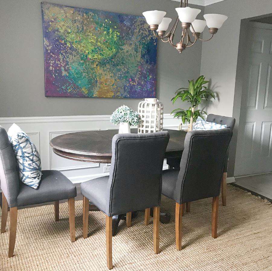 Sala de jantar com paredes cinza, lambris brancos e um grande quadro na parede.