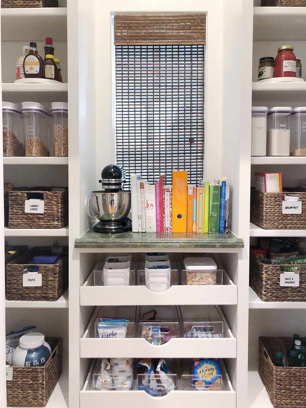 despensa con estanterías organizadas, cestas y una mesa para libros de cocina