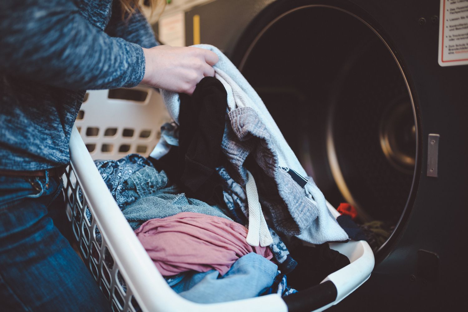 Close-up de uma mulher com um cesto de roupa suja lavando roupas