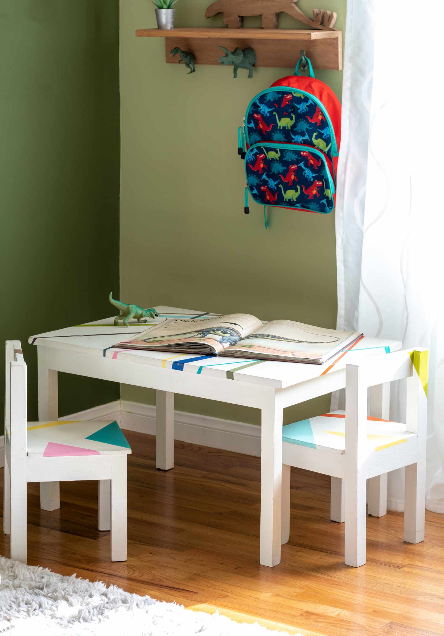 Kinderzimmer mit Dinosaurier-Motiv, bemaltem Schreibtisch und Stühlen