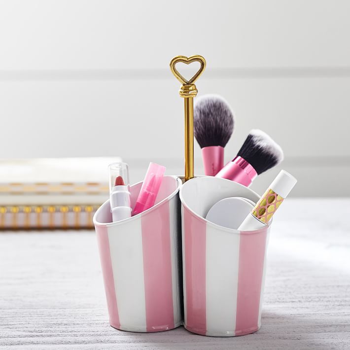 recipientes a rayas rosas y blancas que contienen brochas de maquillaje y pintalabios