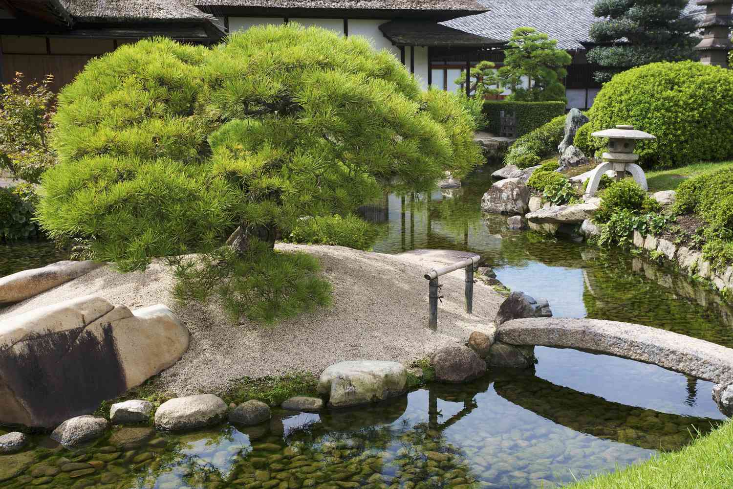 Jardín japonés con agua, plantas y trabajo en piedra.