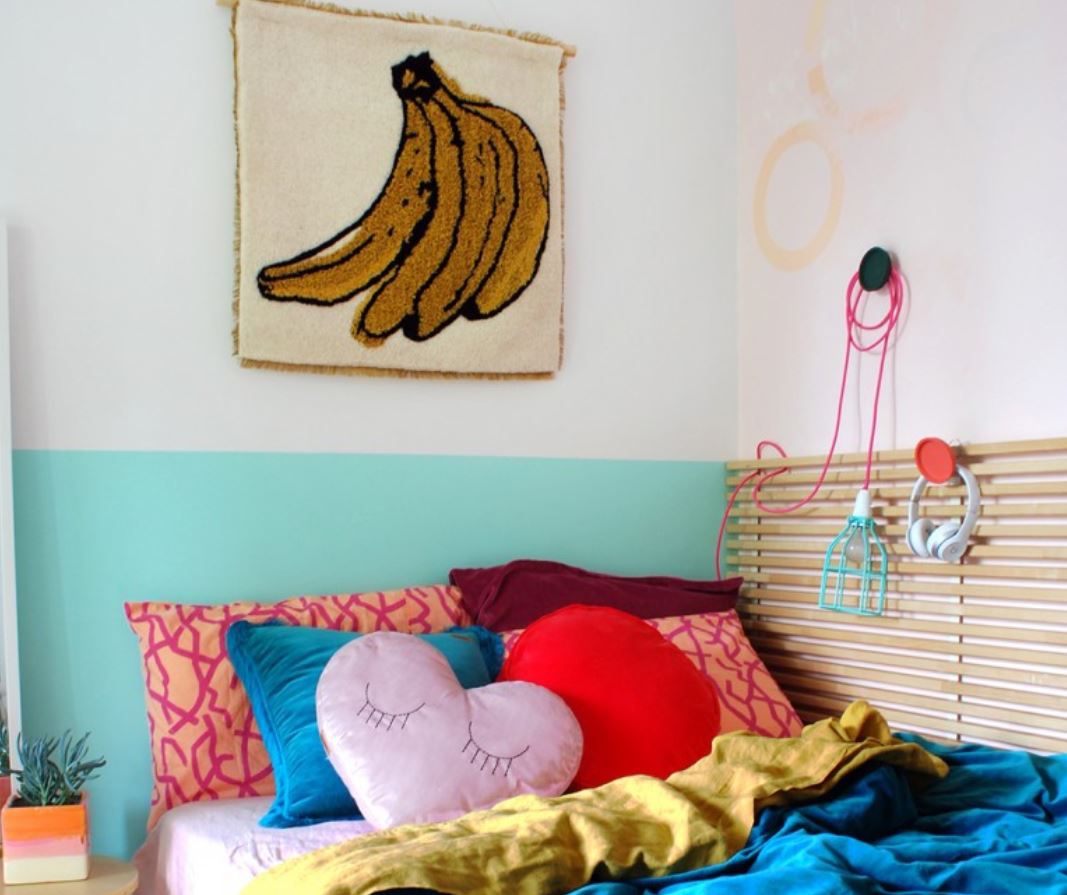 Cama de menina adolescente com muitos travesseiros coloridos e estampa de banana na parede.