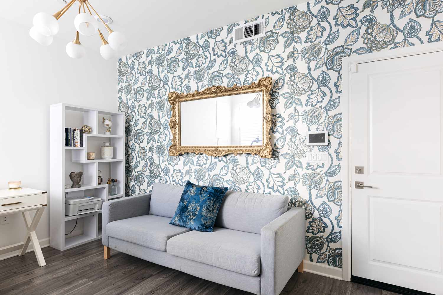 Papel de parede floral branco e azul atrás do sofá cinza