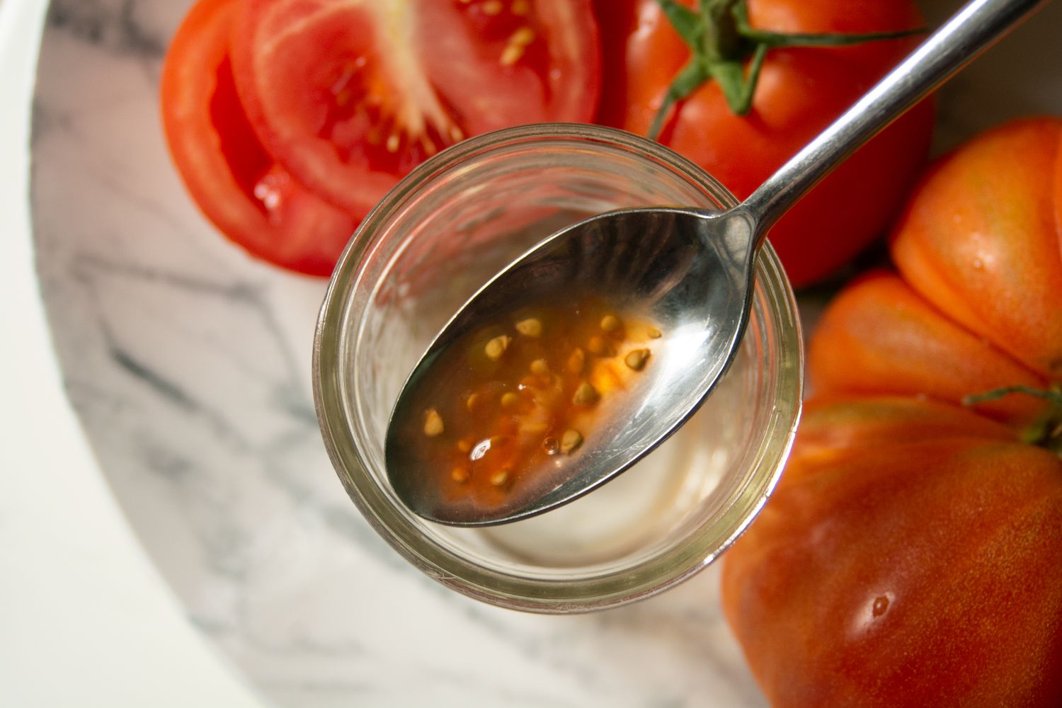 Rote Bio-Tomaten mit Löffel aufgeschnitten, mit Tomatenkernen und Saft in durchsichtigem Becher