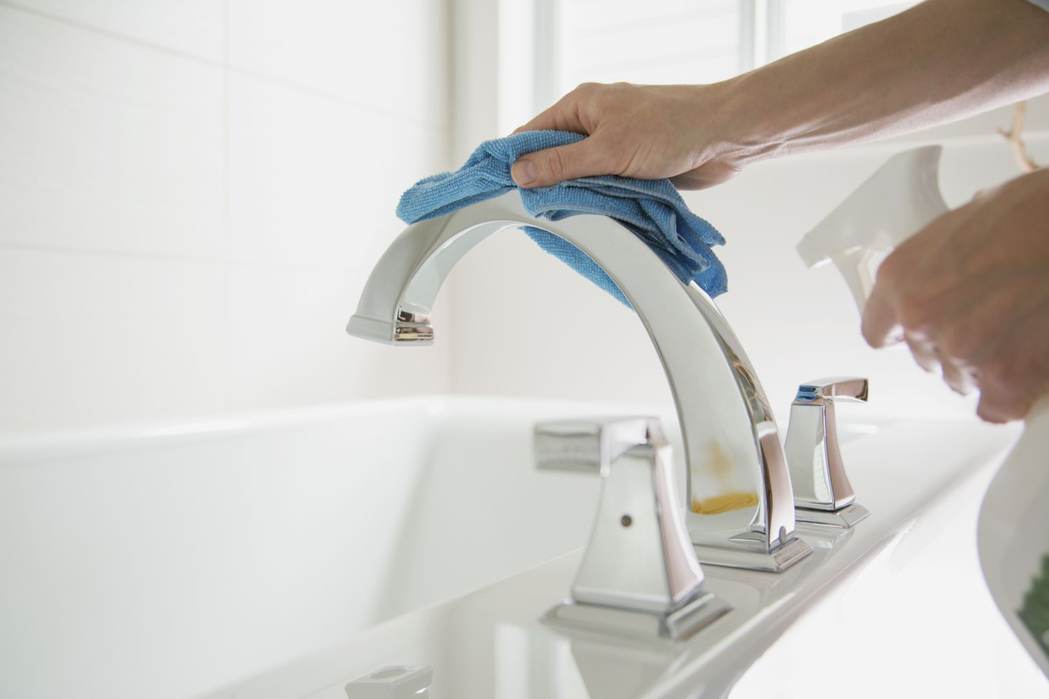 Frau poliert Badezimmerarmatur mit blauem Lappen und Spray.