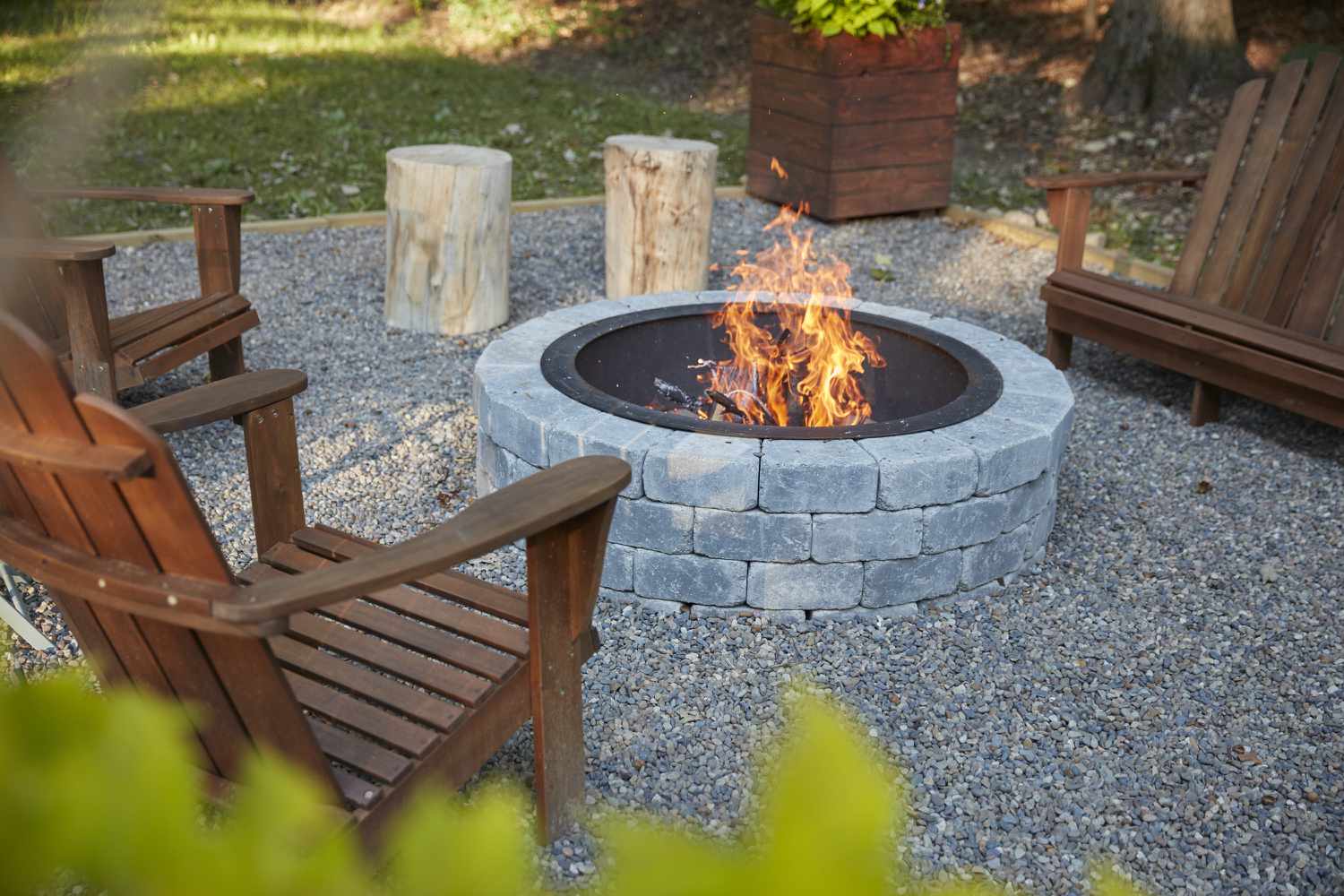 Feuerstelle mit hellgrauen Steinen, umgeben von Holzstühlen und Feuer 