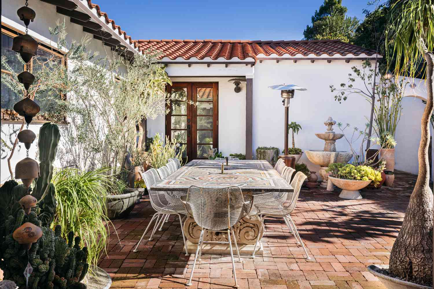 Patio de ladrillo con mesa de comedor al aire libre rodeada de plantas