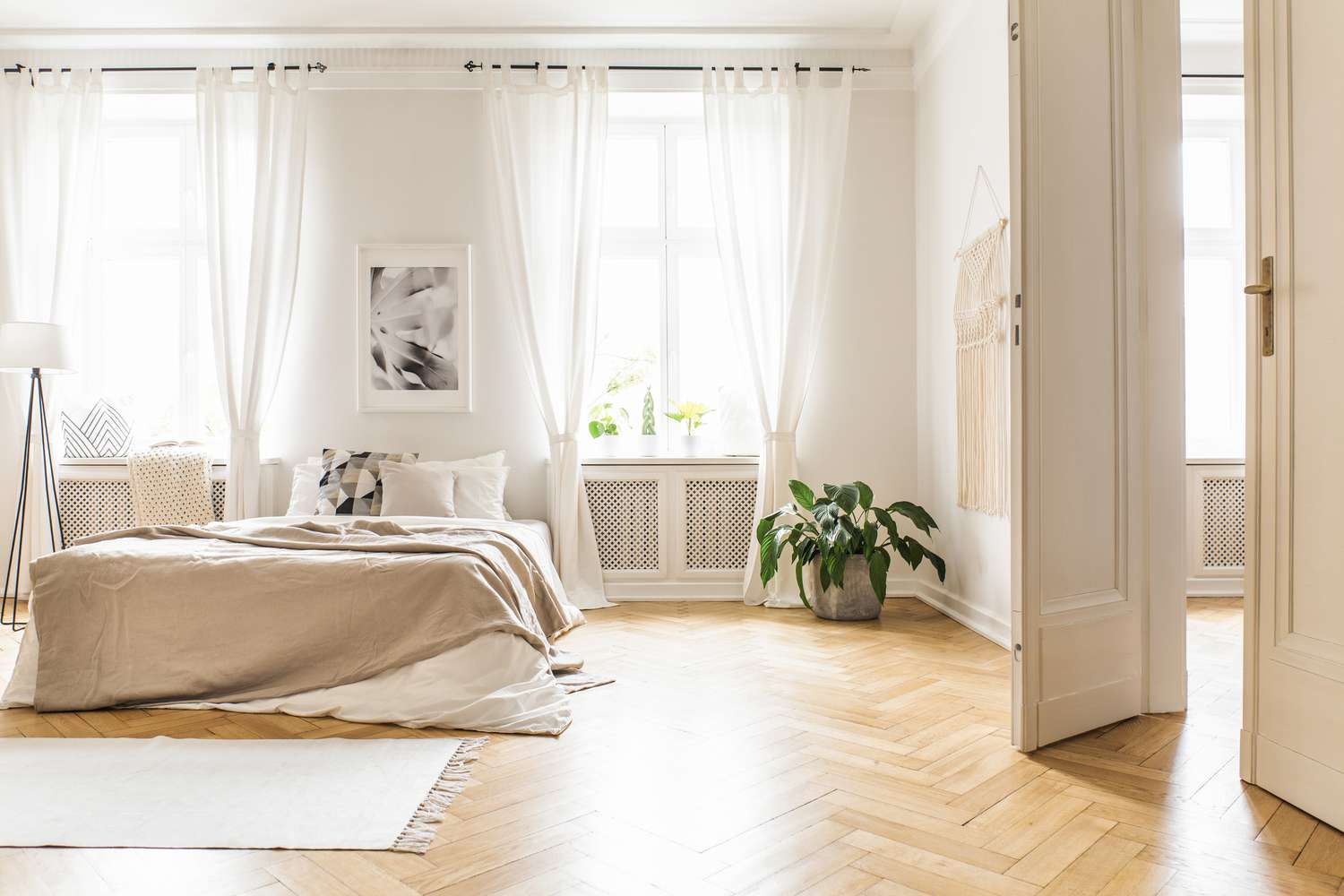 Interior de dormitorio amplio y luminoso con decoración en beige, suelo de madera y un libro en el asiento del alféizar de la ventana