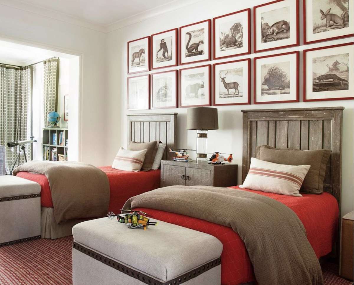 quarto de menino com lençóis vermelhos, cabeceira em tom de madeira médio, paredes brancas, galeria de quadros vermelhos acima da cama