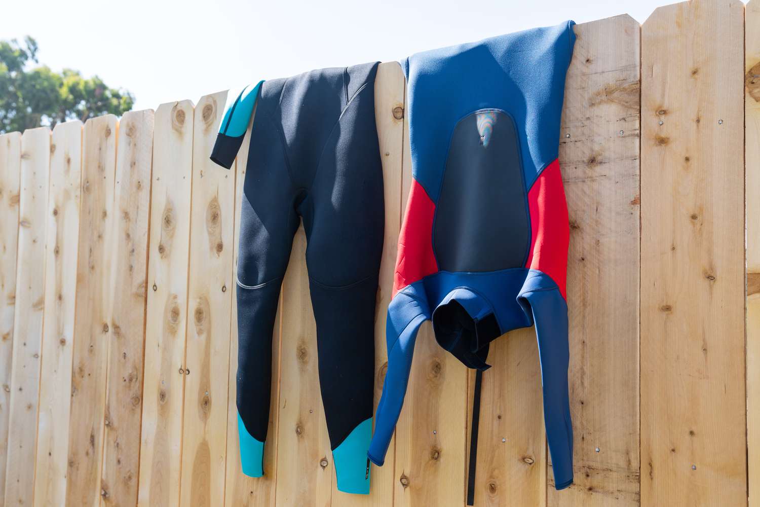 Blue and black wetsuit hanging over wooden fence to air dry