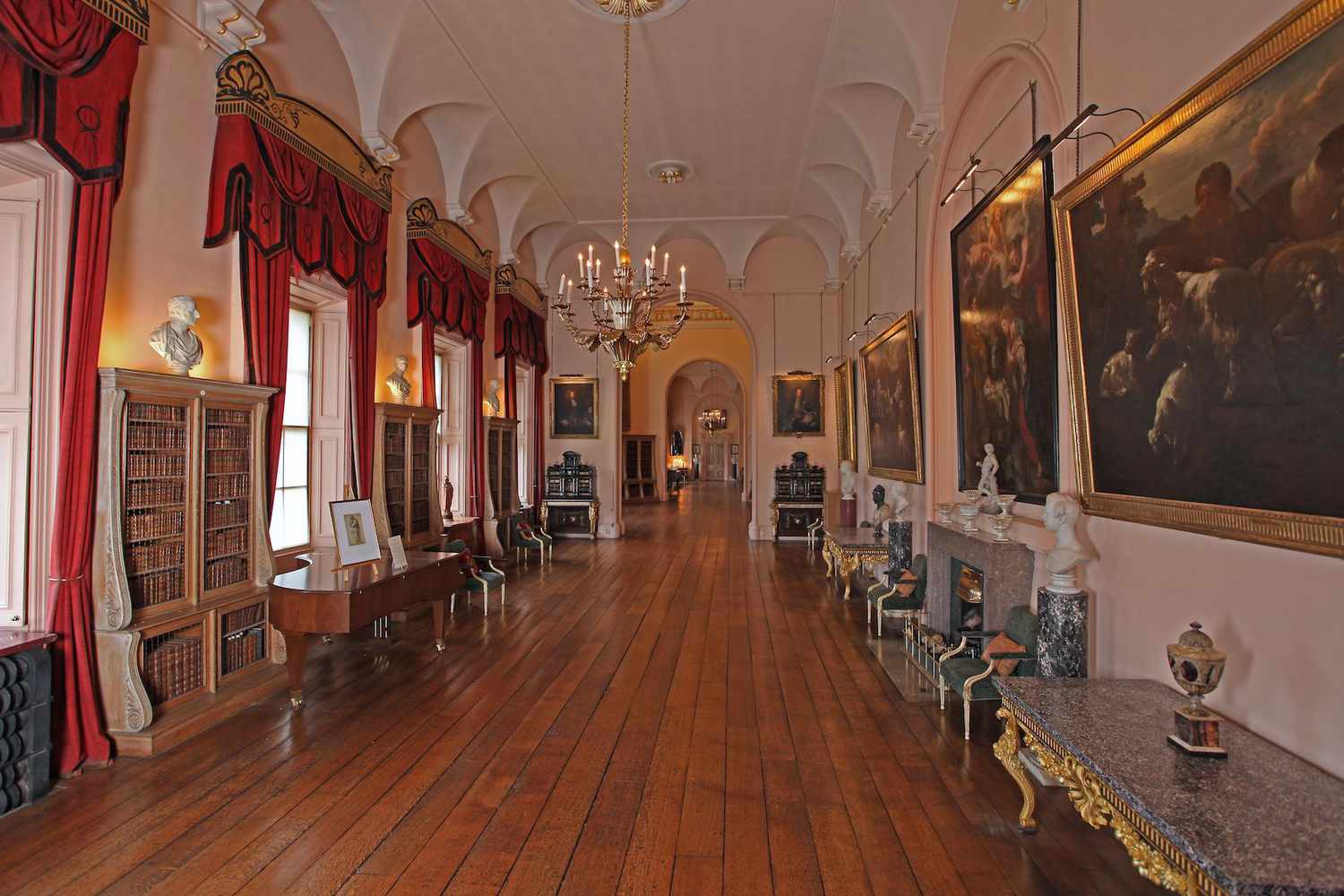 Long Gallery with many books, busts, paintings, and credenzas, and red drapes in Castle Howard