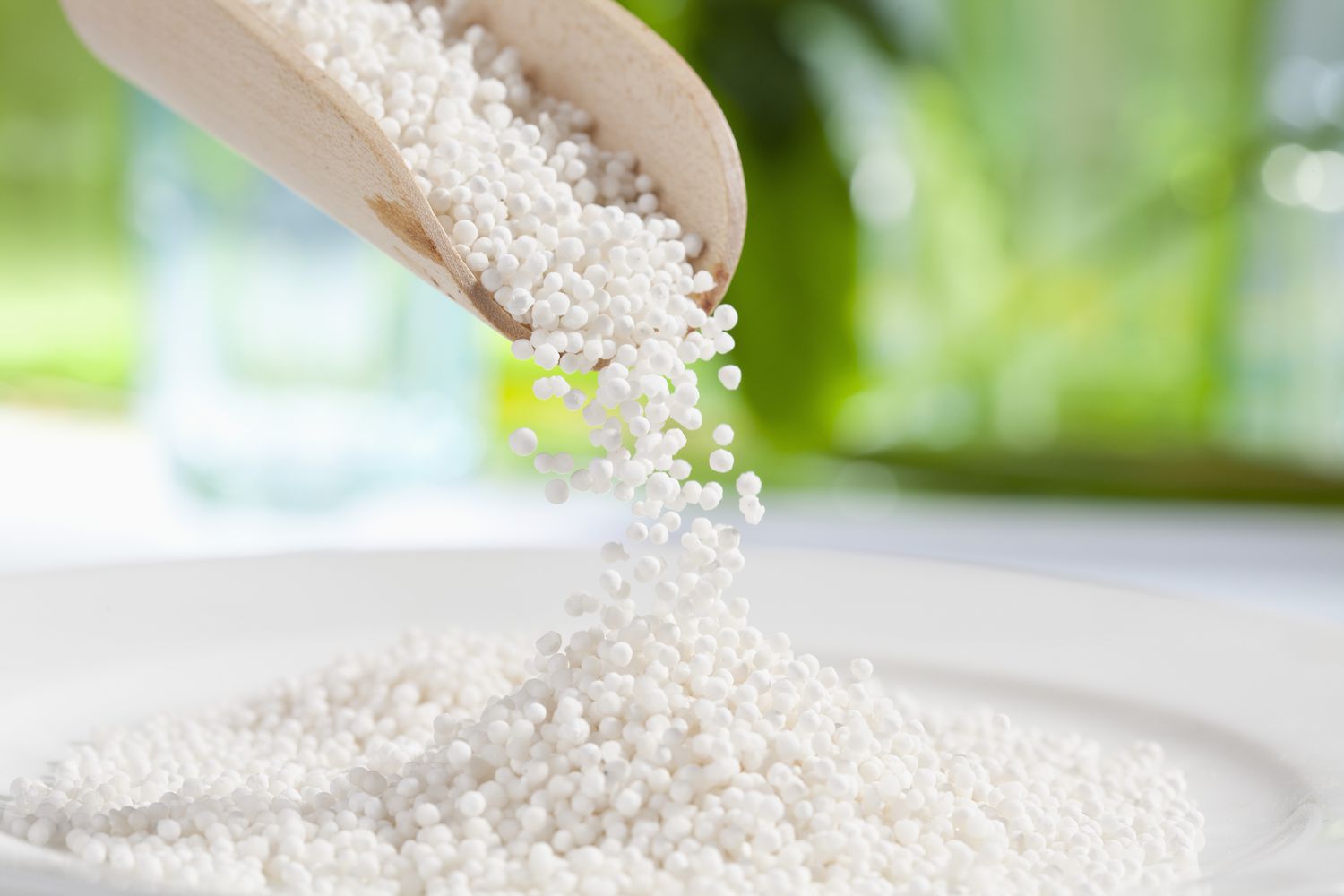 White tapioca pearls falling from a wooden scoop onto a white plate