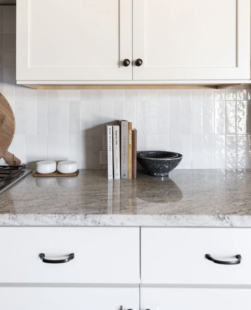 cocina con armarios superiores e inferiores blancos, conjunto de 5 libros de cocina apoyados en la encimera junto a un bol negro