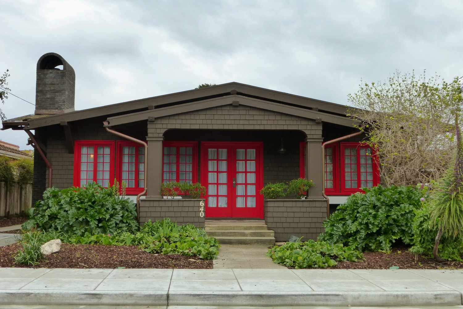 Front view of brown-shingled bungalow with red doors and windows
