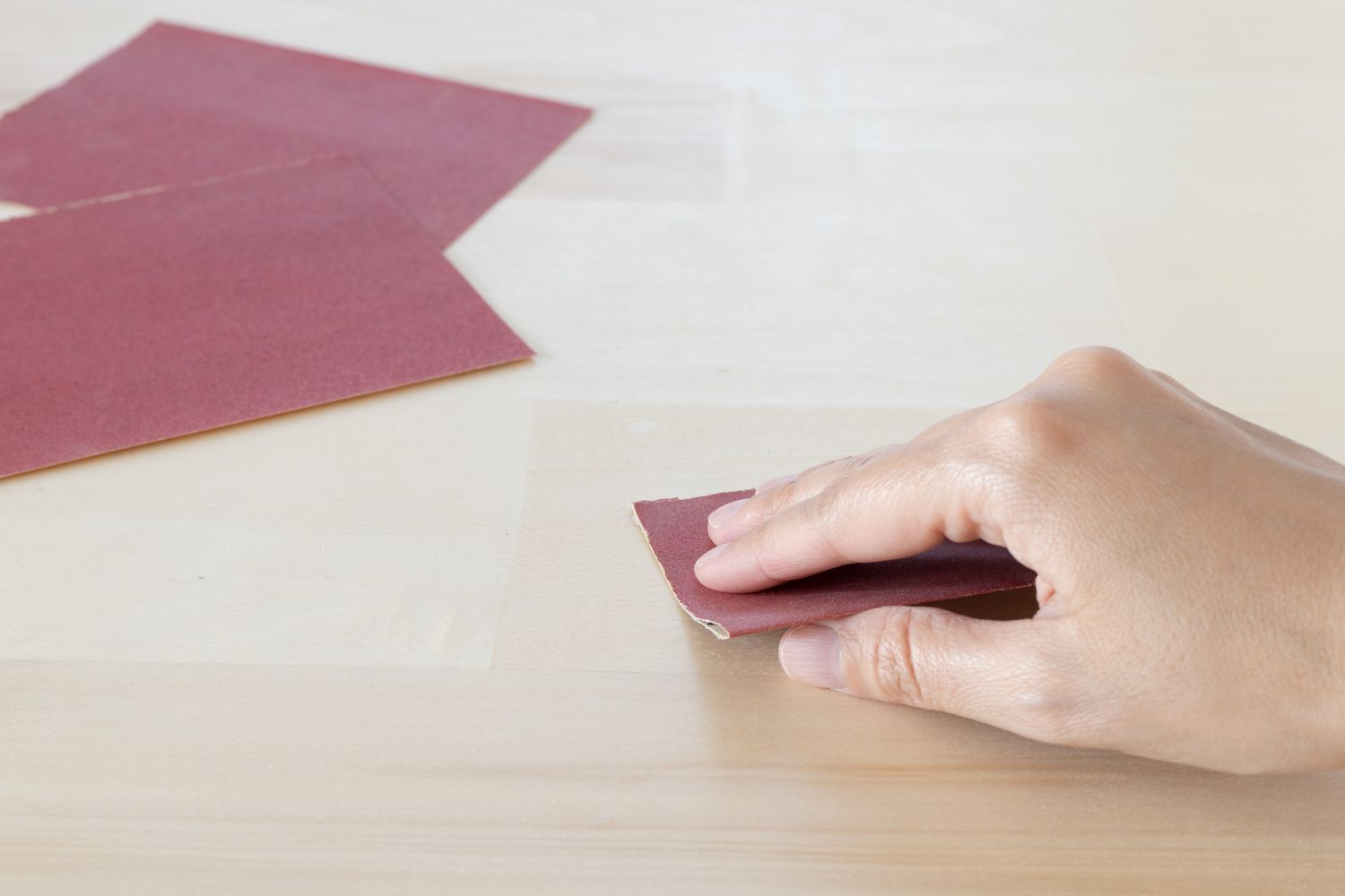 Papier de verre rouge frottant la surface en bois avec de la super colle à la main