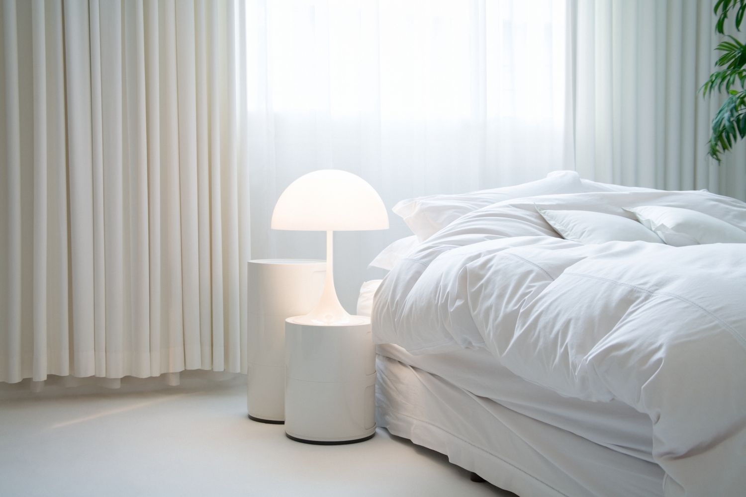 dormitorio blanco con lámpara, cortinas y una planta