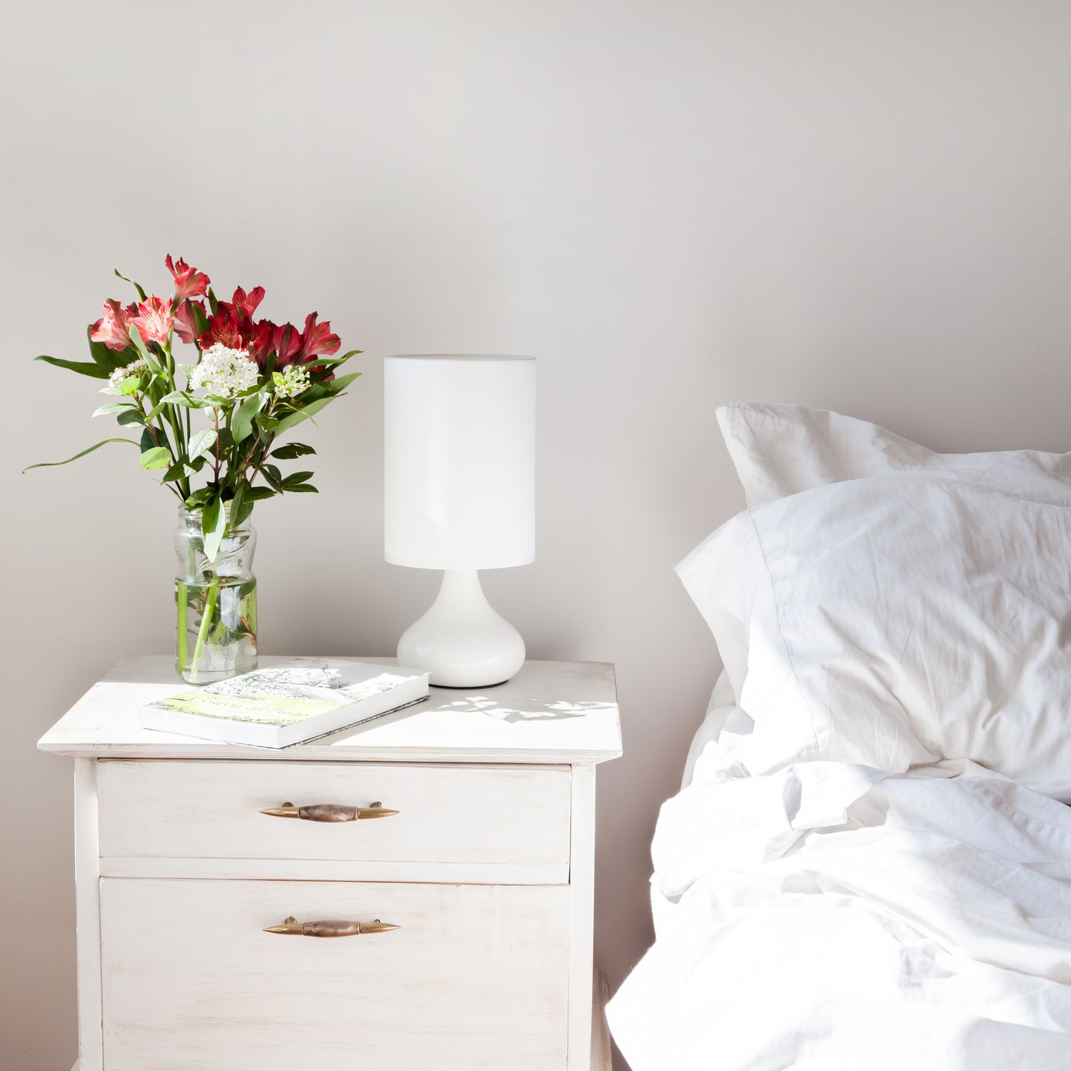 weißes Schlafzimmer mit Blumen auf dem Nachttisch
