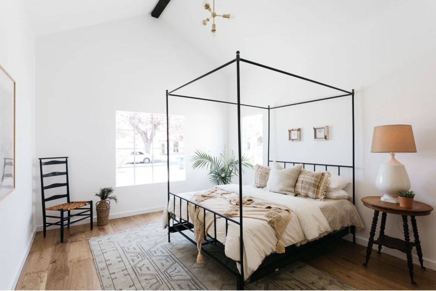 Schlafzimmer mit weißen Wänden und hohen Decken, Holzboden mit einfachem Webteppich, Holznachttisch, Bettgestell mit vier Pfosten, neutrale Farben