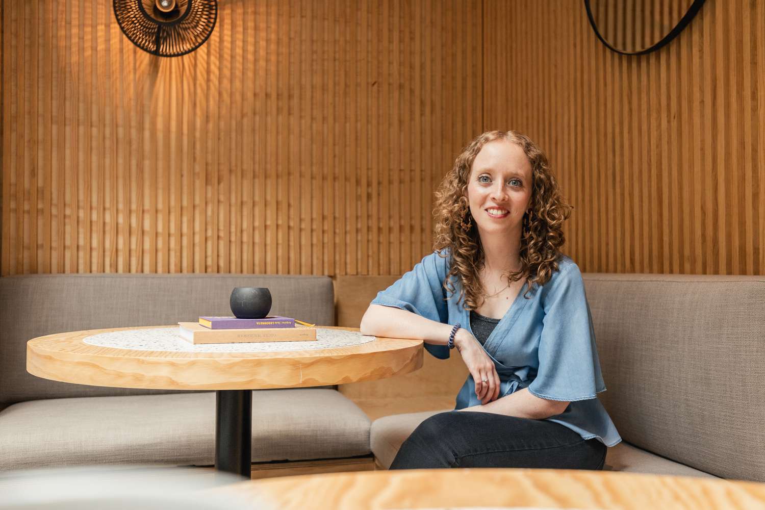 Alexa Backel posiert an einem Holztisch mit einer strukturierten Wand im Hintergrund