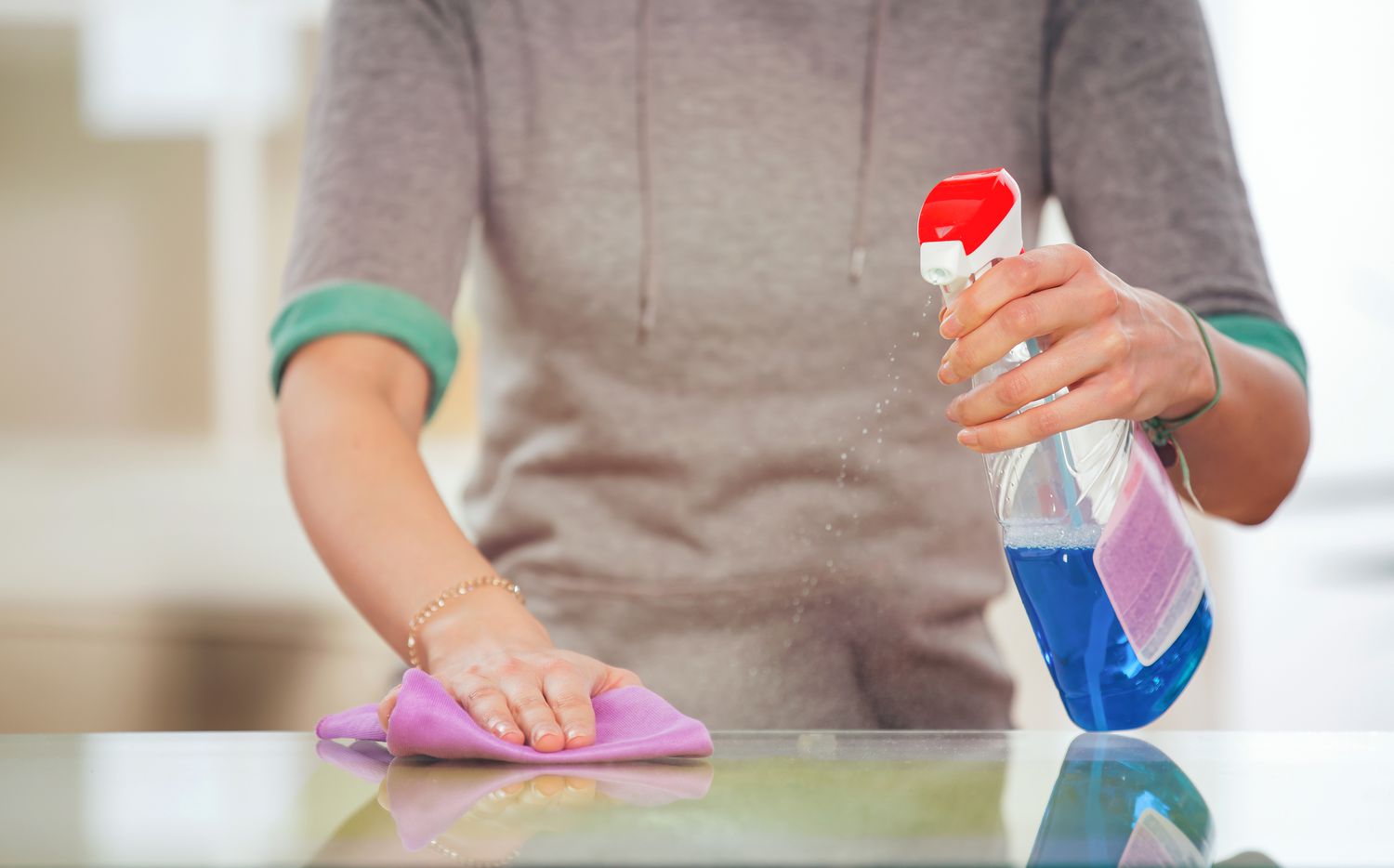 Frau reinigt einen Glastisch mit einem Spray