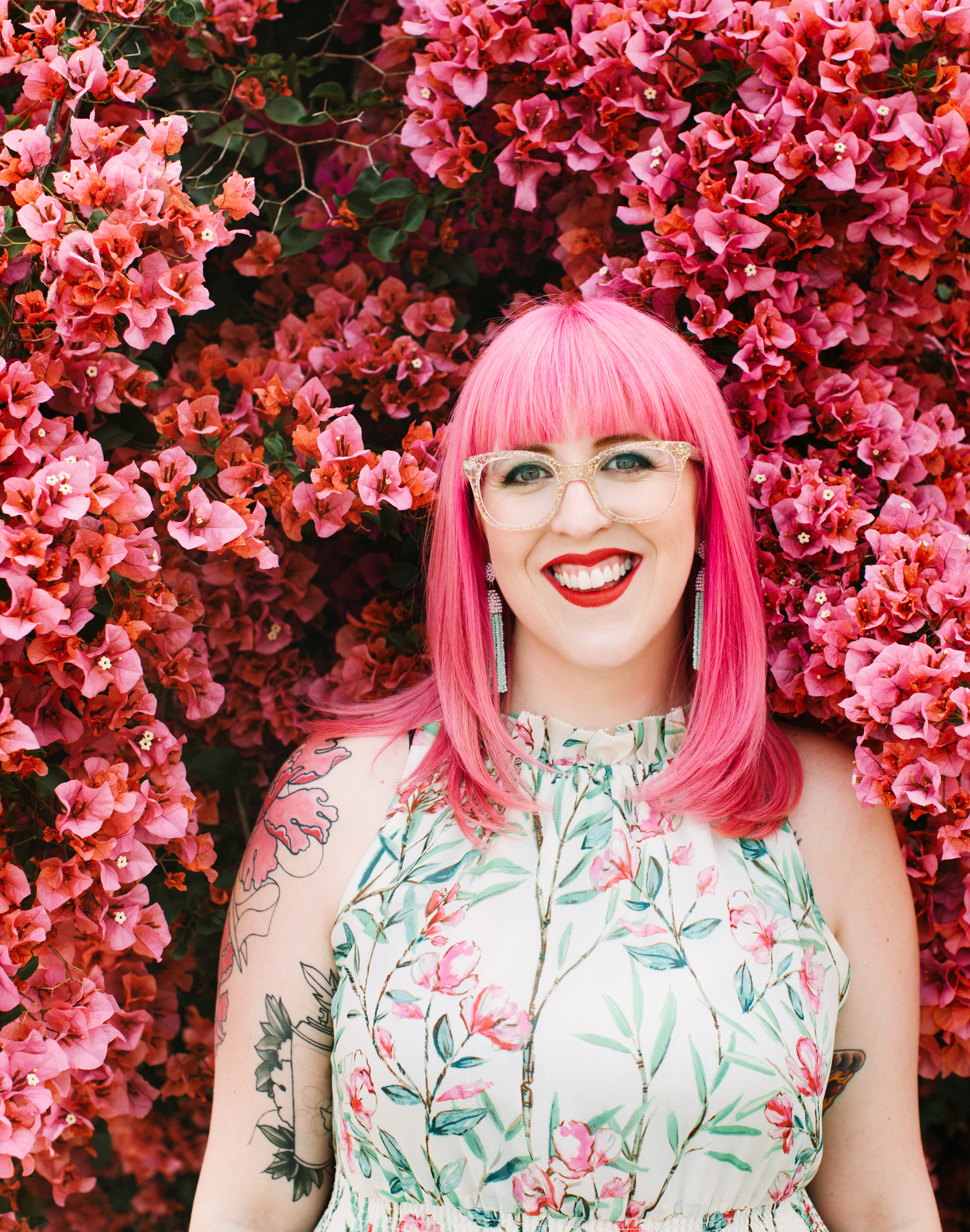 Mulher de cabelo rosa usando vestido com estampa floral em pé em meio a flores rosa