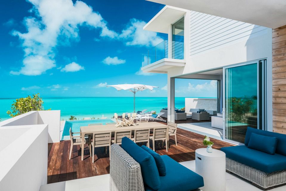 Weißes Strandhaus und Außensitzbereich neben dem offenen Meer mit strahlend blauem Himmel