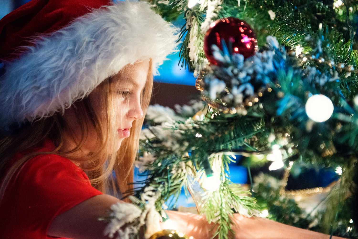 Une petite fille avec un bonnet de Père Noël près du sapin de Noël